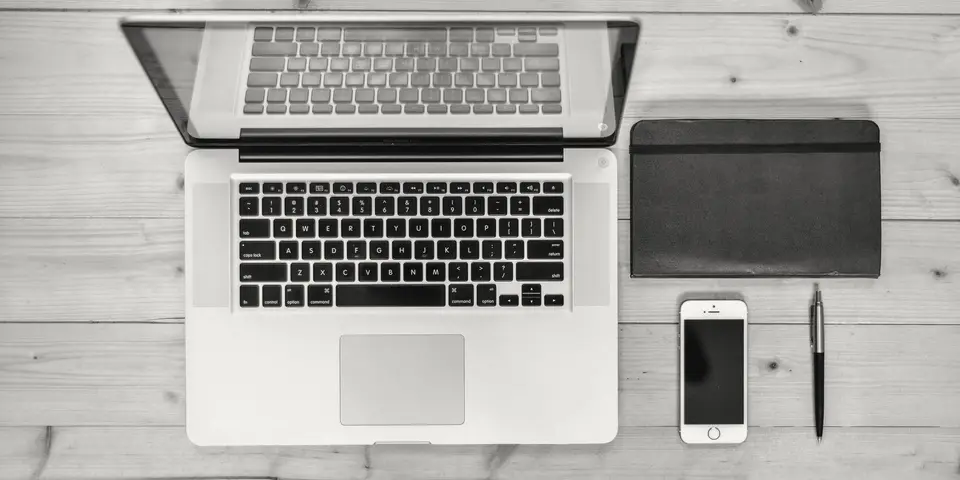 A laptop, smartphone and notebook on a wooden desk